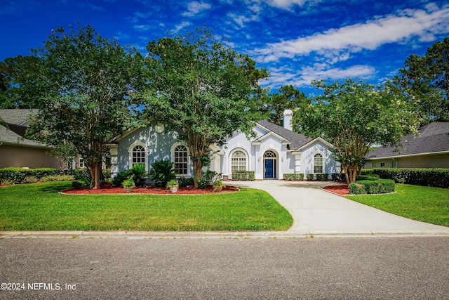 view of front facade featuring concrete driveway, a front lawn, a chimney, and stucco siding