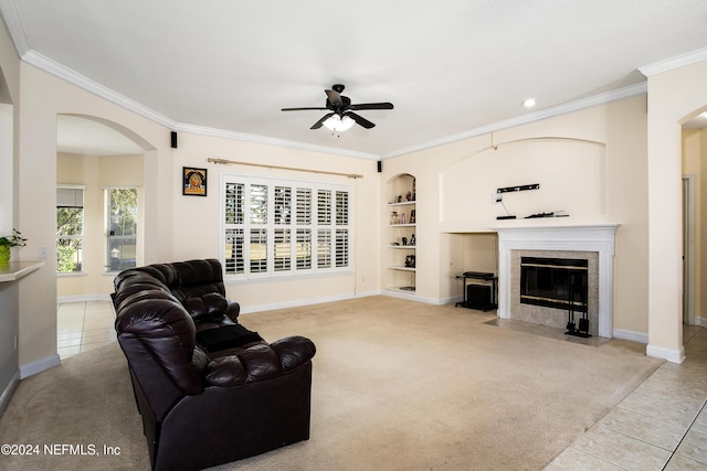 living room featuring a tile fireplace, crown molding, built in shelves, ceiling fan, and light tile patterned floors