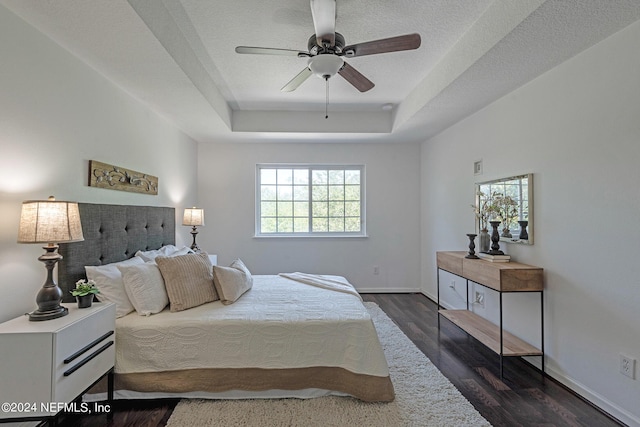 bedroom with dark hardwood / wood-style floors, ceiling fan, a raised ceiling, and a textured ceiling