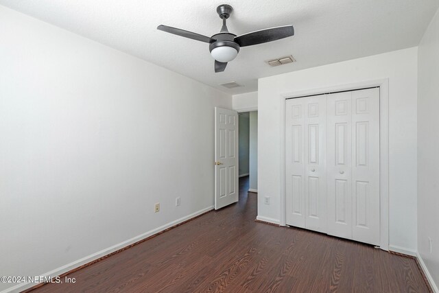 unfurnished bedroom featuring a textured ceiling, ceiling fan, a closet, and dark hardwood / wood-style floors