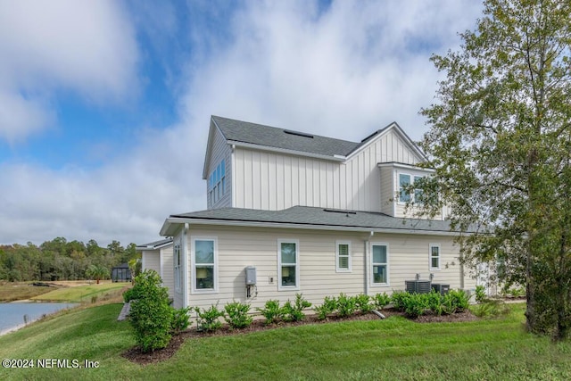 back of house with board and batten siding, a water view, cooling unit, and a lawn