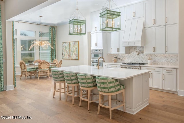 kitchen with custom range hood, backsplash, a kitchen island with sink, a sink, and range