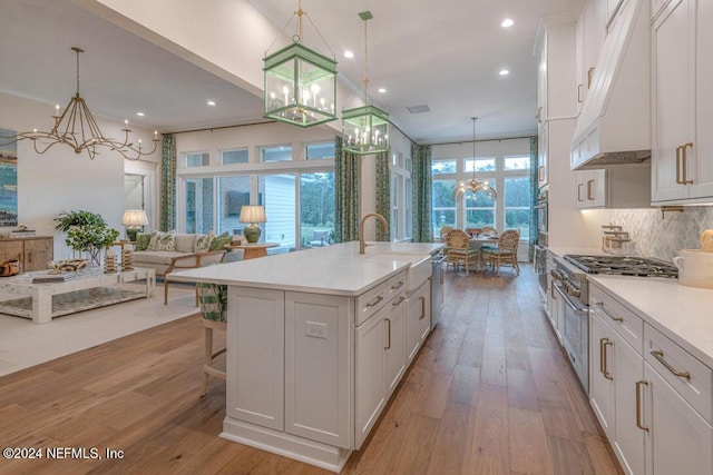 kitchen with light countertops, light wood-style floors, an inviting chandelier, and under cabinet range hood