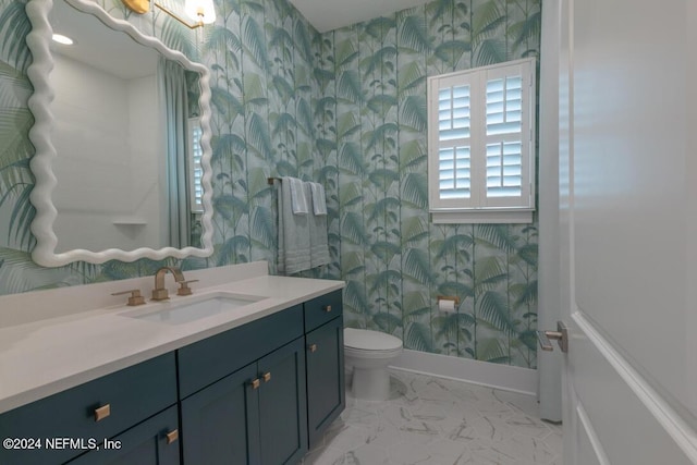 bathroom with toilet, vanity, baseboards, marble finish floor, and wallpapered walls