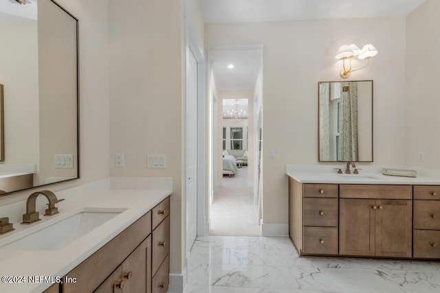 ensuite bathroom featuring marble finish floor, two vanities, a sink, and baseboards