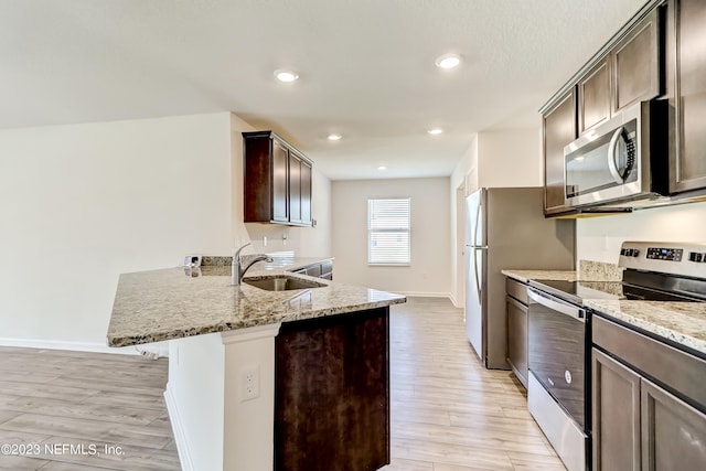 kitchen with light stone counters, stainless steel appliances, light hardwood / wood-style flooring, and sink