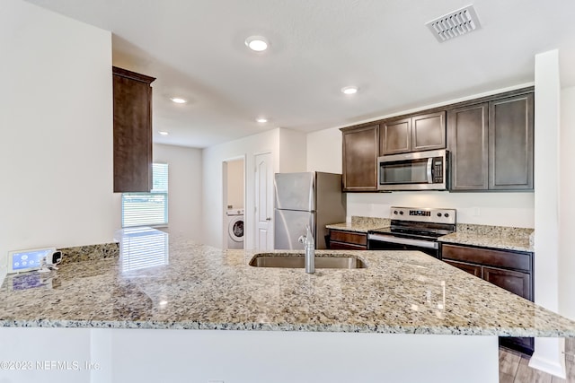 kitchen featuring kitchen peninsula, stainless steel appliances, light stone counters, and sink