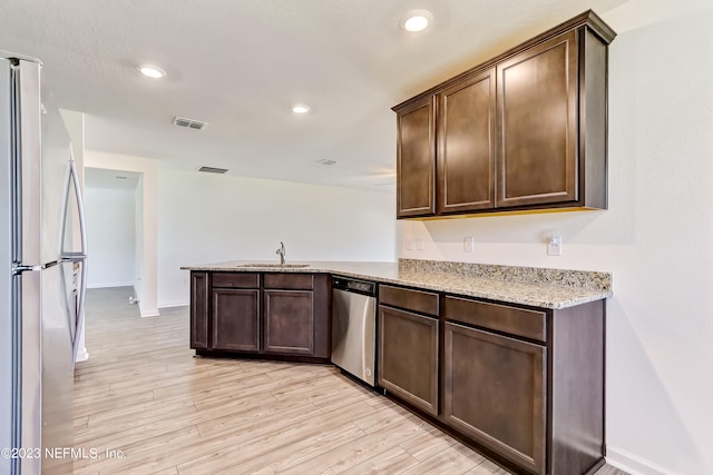 kitchen with kitchen peninsula, light stone countertops, light wood-type flooring, stainless steel appliances, and sink