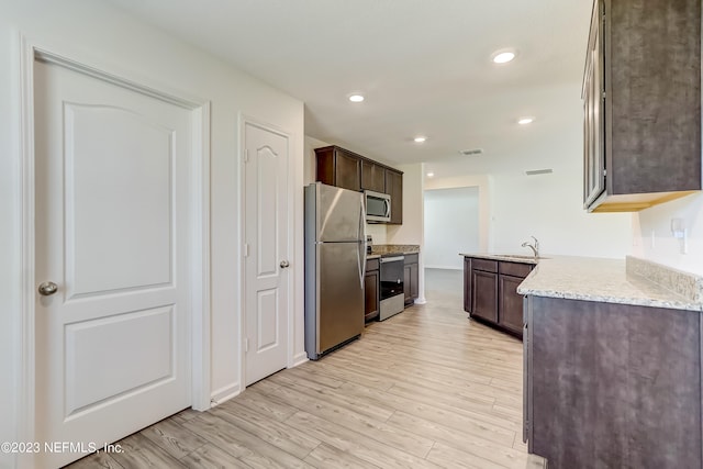 kitchen with light stone countertops, dark brown cabinets, light hardwood / wood-style floors, and appliances with stainless steel finishes