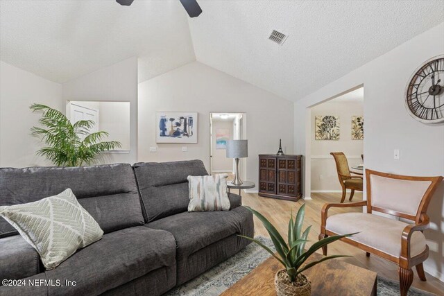 living room with ceiling fan, light hardwood / wood-style flooring, a textured ceiling, and lofted ceiling