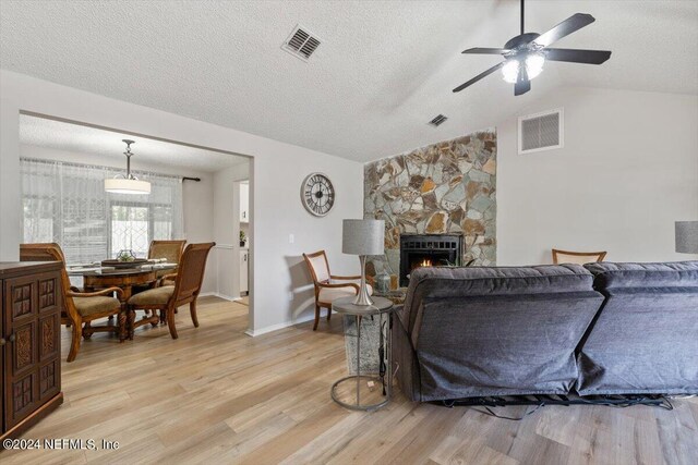 living room featuring ceiling fan, light hardwood / wood-style floors, a fireplace, a textured ceiling, and lofted ceiling