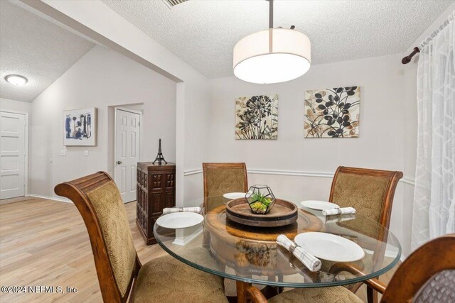 dining space with a textured ceiling, light wood-type flooring, and vaulted ceiling