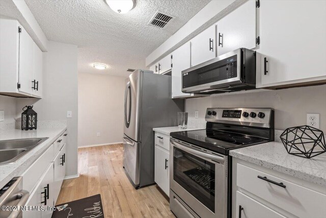 kitchen featuring a textured ceiling, light hardwood / wood-style flooring, appliances with stainless steel finishes, white cabinets, and sink