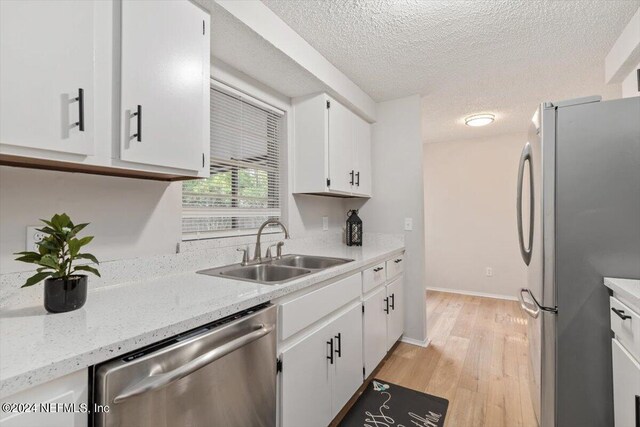 kitchen with a textured ceiling, light hardwood / wood-style flooring, appliances with stainless steel finishes, white cabinets, and sink