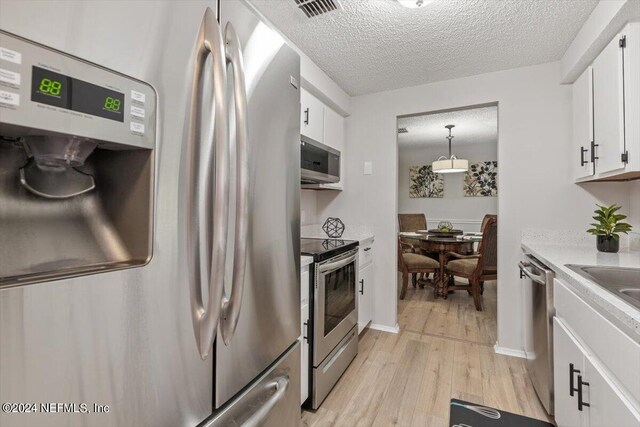 kitchen featuring stainless steel appliances, white cabinetry, light wood-type flooring, and pendant lighting