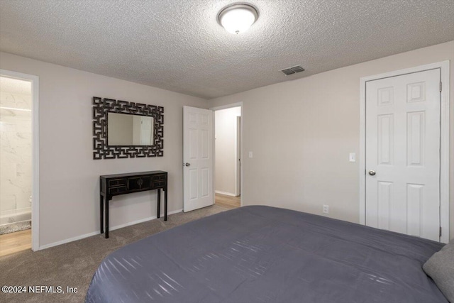 bedroom featuring ensuite bathroom, carpet floors, and a textured ceiling