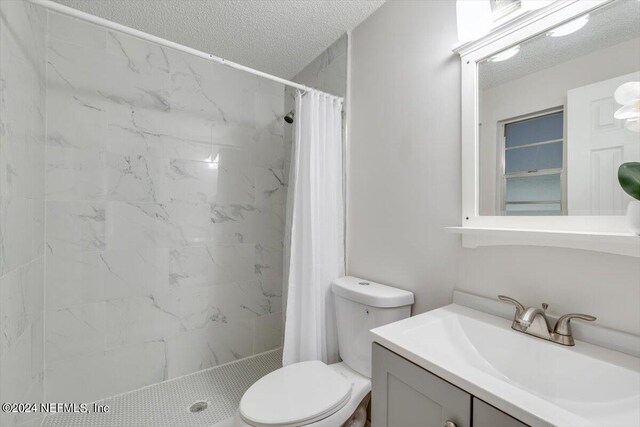 bathroom featuring a shower with shower curtain, vanity, toilet, and a textured ceiling