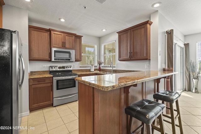 kitchen featuring a kitchen breakfast bar, light tile patterned floors, a textured ceiling, kitchen peninsula, and stainless steel appliances