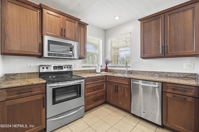 kitchen featuring sink, dark stone counters, a textured ceiling, light tile patterned flooring, and appliances with stainless steel finishes