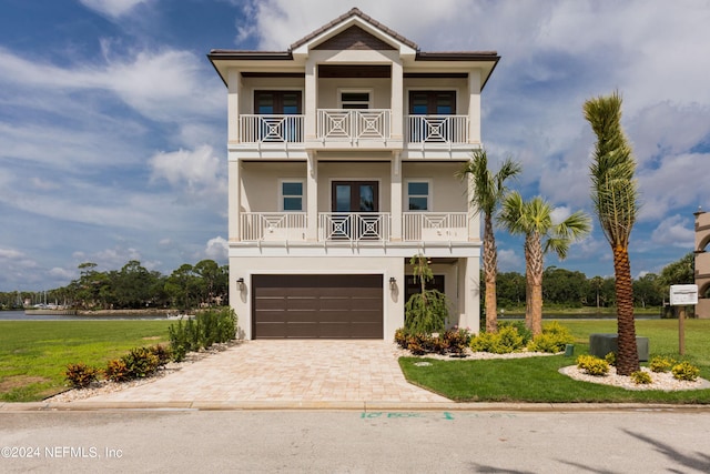 coastal home with a garage, a balcony, decorative driveway, a front lawn, and stucco siding