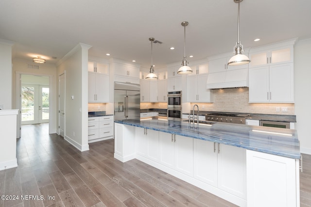 kitchen with stainless steel appliances, a spacious island, wood finished floors, a sink, and white cabinetry