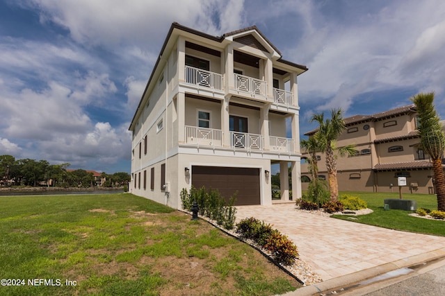 view of front of home with decorative driveway, a balcony, a front lawn, and stucco siding