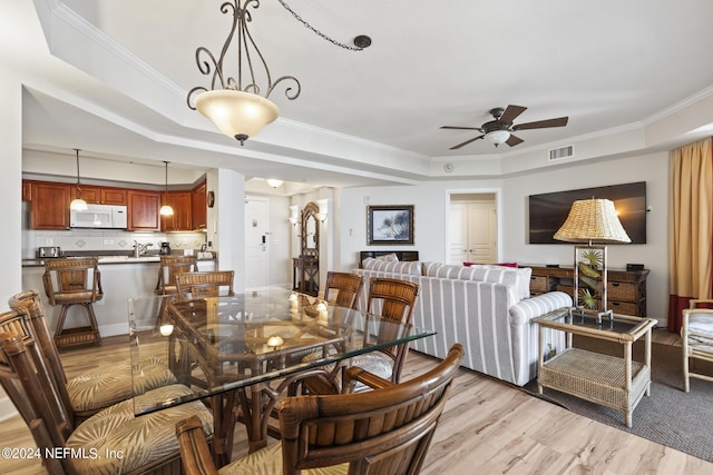 dining space with crown molding, light hardwood / wood-style flooring, a raised ceiling, and ceiling fan