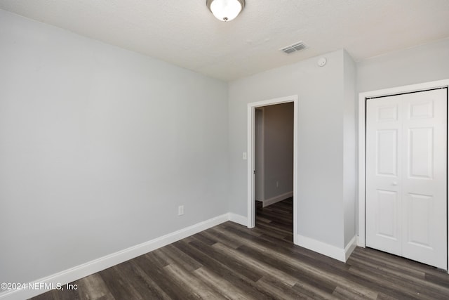 unfurnished bedroom with dark hardwood / wood-style floors, a textured ceiling, and a closet