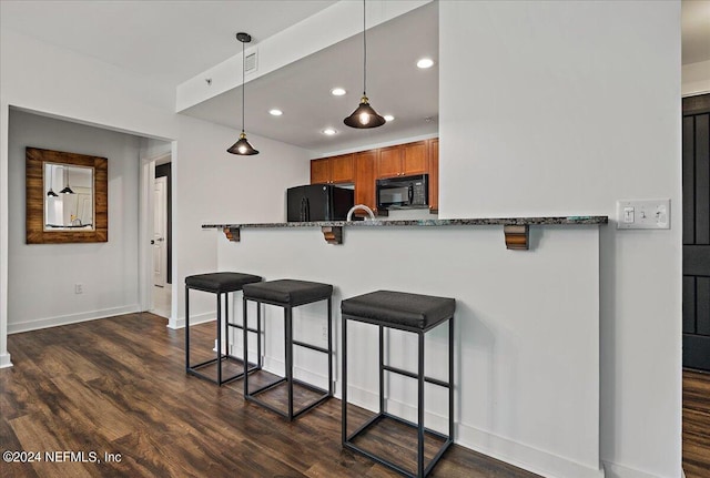 kitchen featuring kitchen peninsula, a kitchen breakfast bar, dark hardwood / wood-style flooring, dark stone counters, and black appliances