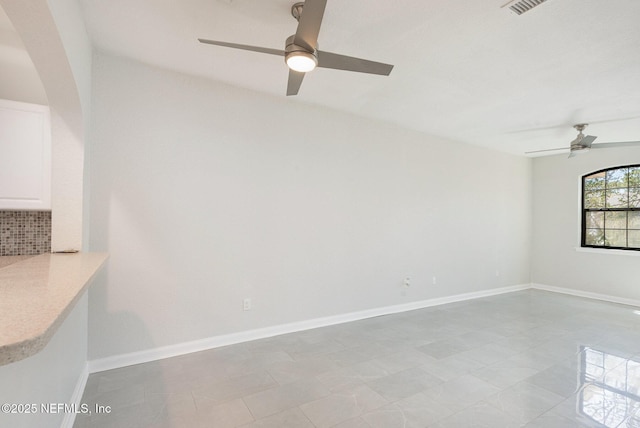 spare room featuring arched walkways, visible vents, baseboards, and ceiling fan