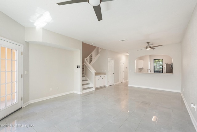 unfurnished living room featuring visible vents, a ceiling fan, stairway, arched walkways, and baseboards