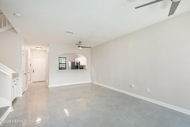 unfurnished living room featuring arched walkways, visible vents, baseboards, and ceiling fan