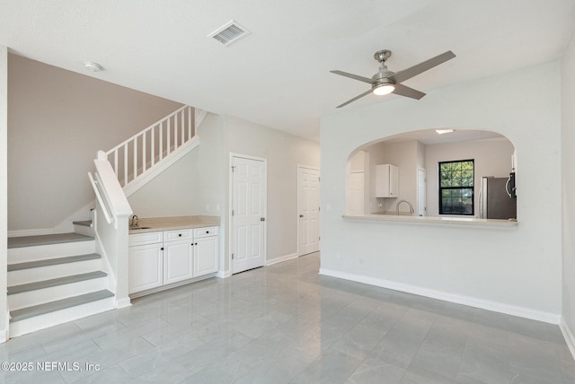 unfurnished living room featuring stairway, baseboards, visible vents, arched walkways, and ceiling fan