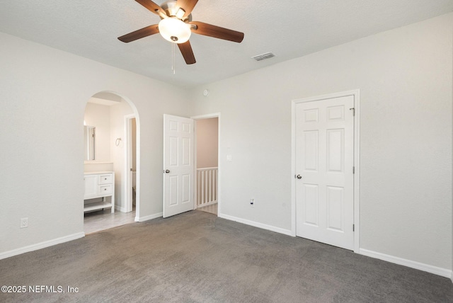 unfurnished bedroom with visible vents, arched walkways, dark colored carpet, and baseboards