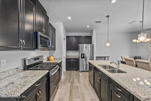 kitchen with pendant lighting, sink, stainless steel appliances, light stone counters, and light hardwood / wood-style floors