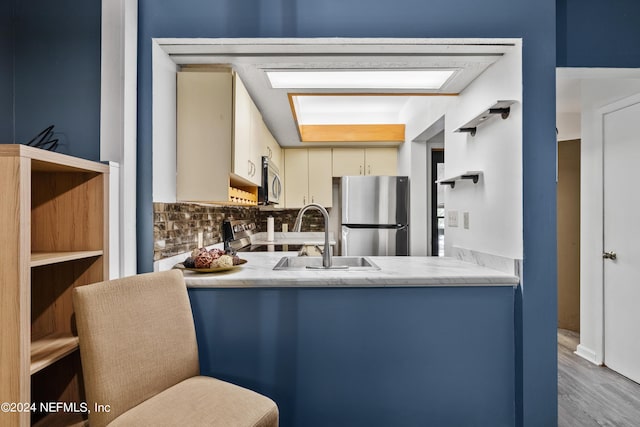 kitchen with sink, tasteful backsplash, light hardwood / wood-style flooring, cream cabinets, and appliances with stainless steel finishes