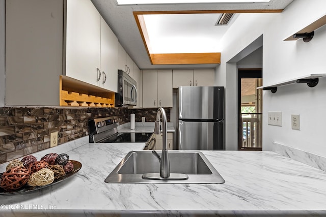 kitchen with decorative backsplash, stainless steel appliances, light stone countertops, and sink