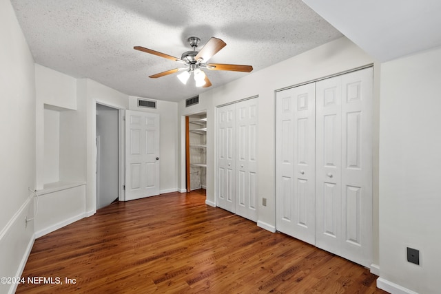 unfurnished bedroom with ceiling fan, dark hardwood / wood-style floors, a textured ceiling, and two closets