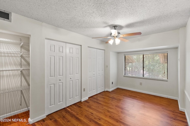 unfurnished bedroom with wood-type flooring, a textured ceiling, ceiling fan, and multiple closets