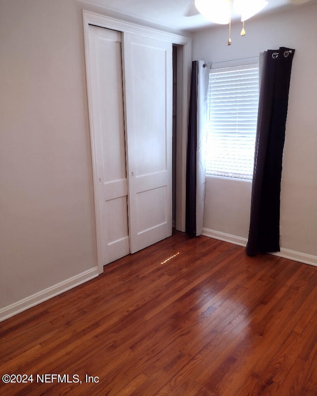 unfurnished bedroom featuring dark wood-style floors, a closet, and baseboards