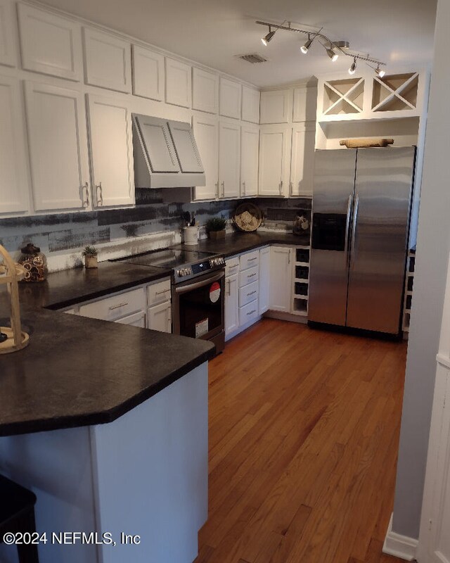 kitchen with dark countertops, appliances with stainless steel finishes, white cabinetry, a peninsula, and wall chimney exhaust hood