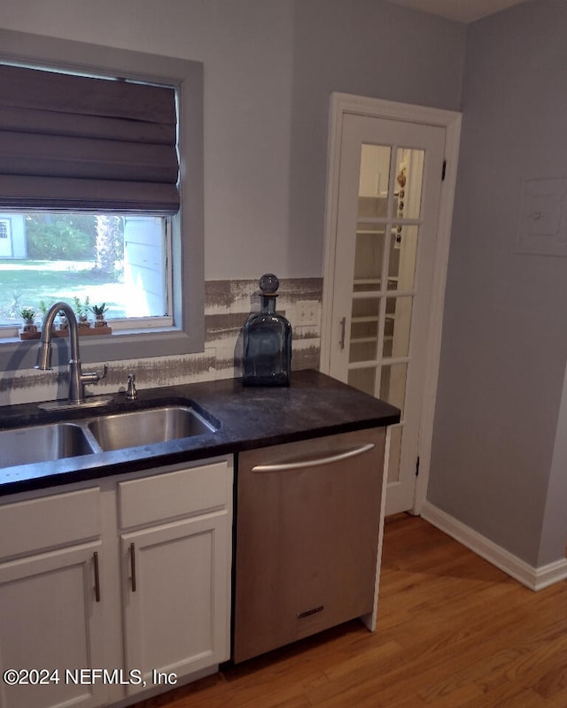 kitchen featuring dishwasher, dark countertops, light wood-style flooring, white cabinetry, and a sink