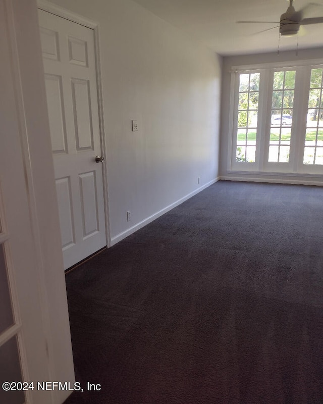 empty room featuring baseboards, dark colored carpet, and a ceiling fan