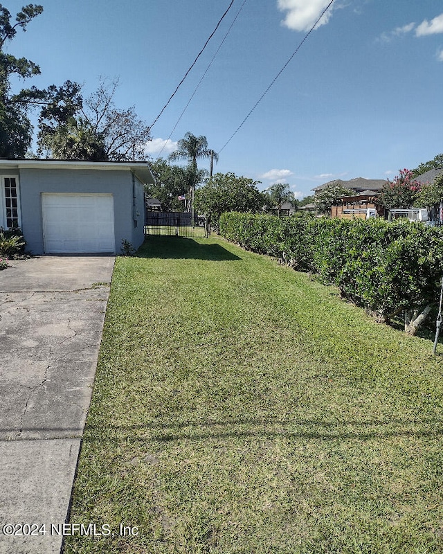 view of yard featuring a garage, concrete driveway, and fence