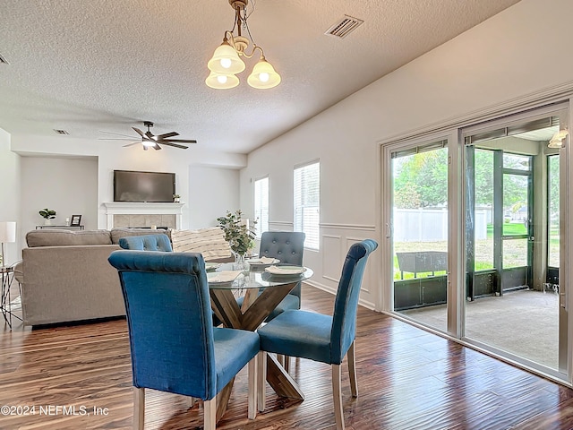 dining space featuring a textured ceiling, a tile fireplace, wood-type flooring, and ceiling fan with notable chandelier