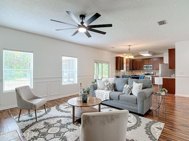 living room with a textured ceiling, ceiling fan with notable chandelier, and dark wood-type flooring