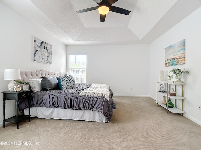 carpeted bedroom featuring a tray ceiling, ceiling fan, and a textured ceiling