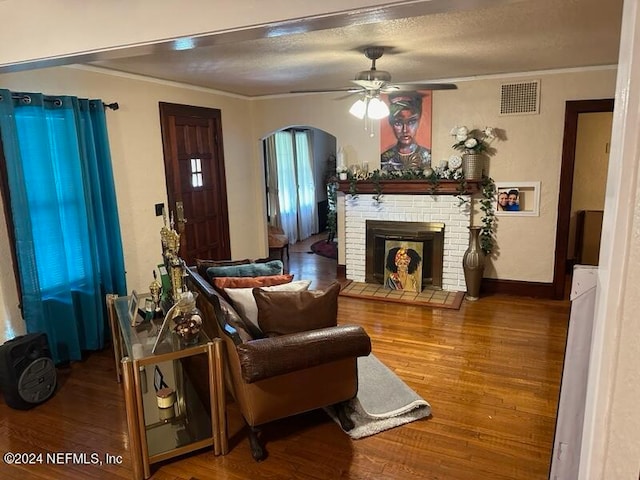 living room with wood-type flooring, ornamental molding, ceiling fan, and a brick fireplace