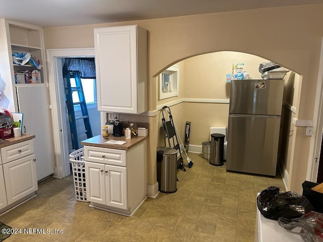 kitchen featuring freestanding refrigerator, white cabinetry, arched walkways, and baseboards