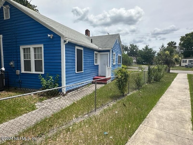 view of side of home with a fenced front yard, a chimney, and a shingled roof